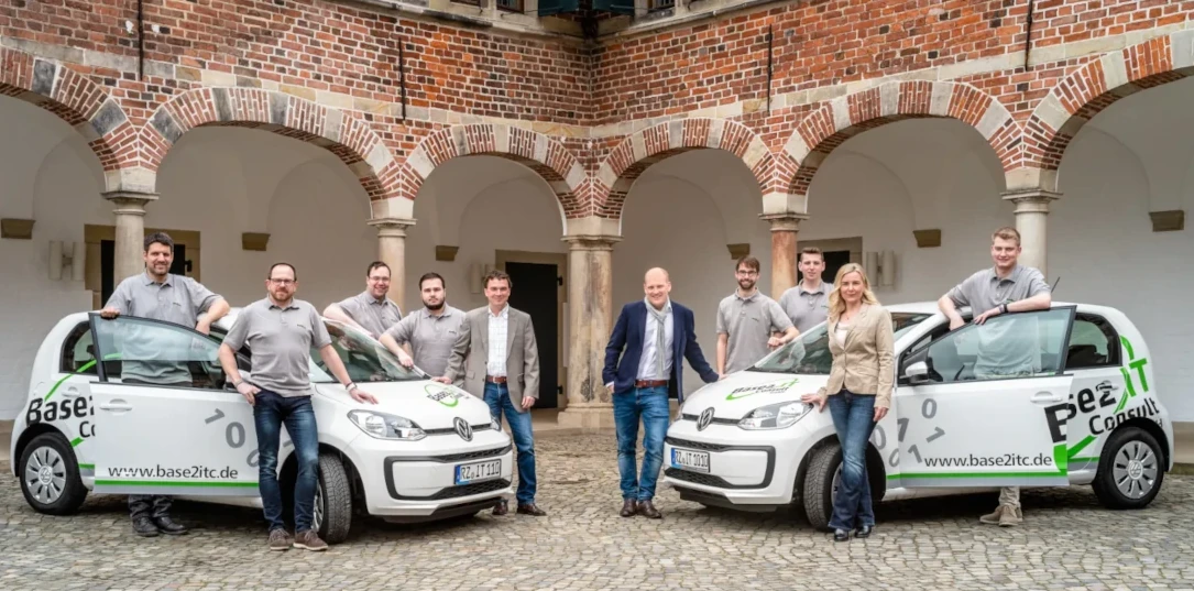 IT-Consulting Team vor Firmenautos im Innenhof mit Backsteinarkaden
